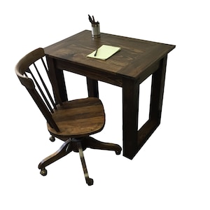 May include: A dark brown wooden desk and matching chair set. The desk has a square top with a recessed border and is approximately 30 inches wide. The chair is a swivel style with a curved back and caster wheels. A notepad and pens sit on the desk.