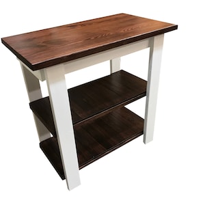 May include: A wooden table with two shelves. The table top and shelves are a dark brown wood stain. The legs and frame are painted white.