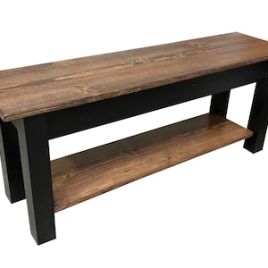 May include: A wooden bench with a black base and a lower shelf. The bench has a natural wood finish and is made of solid wood.