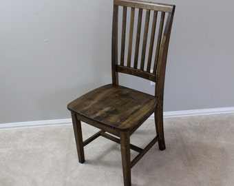 May include: A wooden dining chair with a dark brown finish. The chair features a slatted back and a square seat. The legs are straight and sturdy, and the chair is designed for everyday use. The chair is made of solid wood.