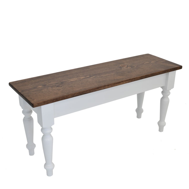 Puede incluir: Un banco de madera blanco con una tapa te&ntilde;ida de color marr&oacute;n oscuro y patas torneadas. El banco est&aacute; hecho de madera maciza y tiene un estilo sencillo de granja.