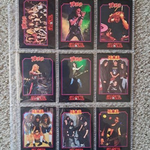 May include: Nine collectible trading cards featuring the band Dio, displayed in a clear plastic sheet. Each card has a black background with a pink border and the band's logo. The cards feature images of the band members performing. The text "MEGA METAL" is visible on each card.