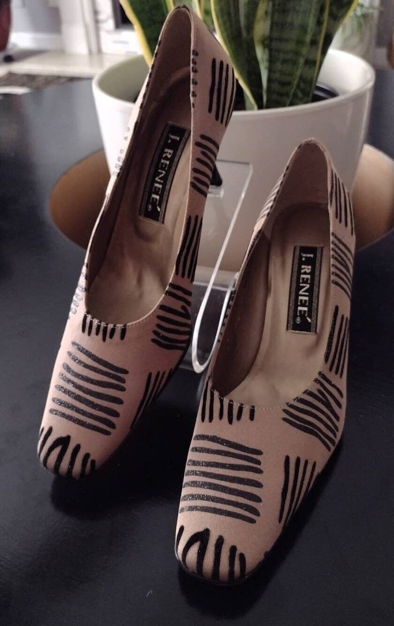 May include: A pair of J. Renee heels with a light brown fabric and black striped pattern. The shoes have a low heel and a pointed toe. The brand name is visible on the insole.