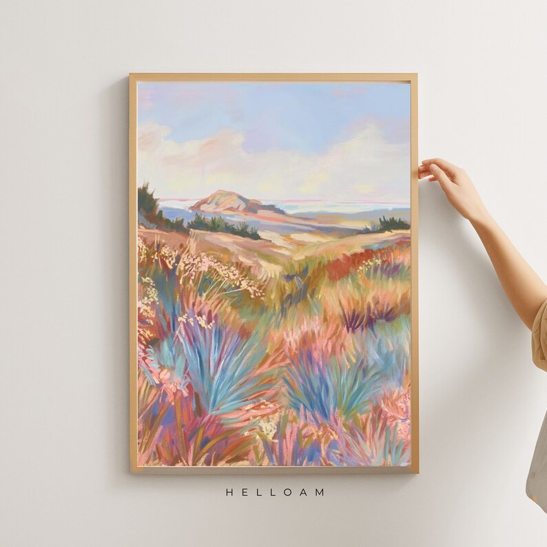 Peut inclure: Une peinture repr&eacute;sentant un paysage avec une colline au loin et un champ de fleurs color&eacute;es au premier plan. Le ciel est bleu avec des nuages blancs. La peinture est encadr&eacute;e dans un cadre en bois clair.