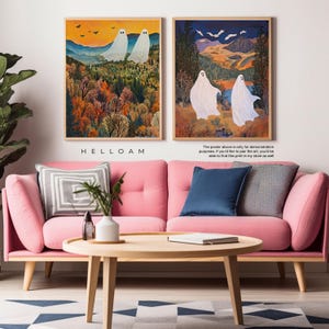 May include: Two digital art prints of white ghosts in a forest setting. The first print features two ghosts in a forest with fall foliage. The second print features two ghosts walking in a forest with a blue sky and mountains in the background. The prints are framed in wood and are displayed on a pink sofa with a coffee table.
