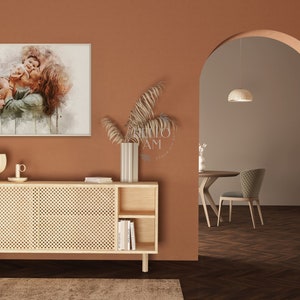 May include: A watercolor painting of a couple embracing, displayed on a wall above a light wood cabinet with a woven rattan front. The cabinet has two doors and two open shelves. A vase with dried branches sits on top of the cabinet.