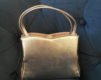May include: A gold metallic handbag with a single top handle and a decorative clasp.