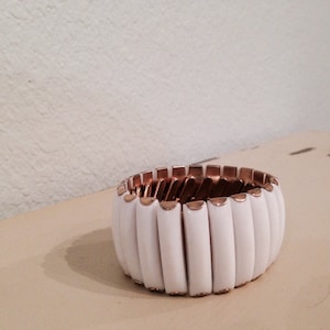 May include: White and gold expandable bracelet with a series of white ceramic links. The bracelet is made of metal and has a simple, modern design.