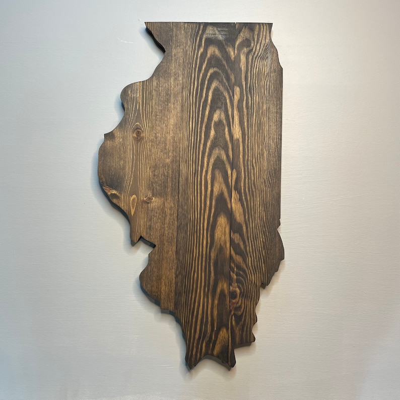 Puede incluir: Adorno de pared de madera con la forma del estado de Illinois. La madera tiene un tinte marr&oacute;n oscuro, con vetas visibles. Montado en una pared gris claro, resalta el contorno del estado. Mide aproximadamente 76 cm de alto.