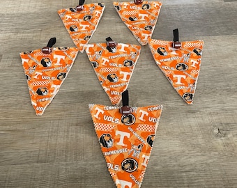 May include: Seven orange and white triangular fabric pennants with the words "Tennessee Vols" and a cartoon mascot printed on them. Each pennant has a small brown football attached to the top.