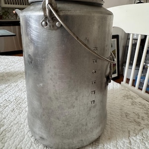 May include: A vintage aluminum coffee percolator with a clear glass top and a metal handle. The pot has measurement markings and a hinged lid. The percolator is a classic kitchen item.