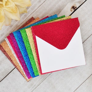 May include: A stack of colorful glitter envelopes with white interiors. The envelopes are arranged in a fan shape, with the red envelope on top. The envelopes are perfect for adding a touch of sparkle to any occasion.