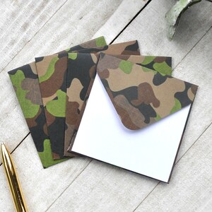 May include: Set of four camouflage patterned envelopes with white paper inserts. The envelopes are folded and stacked on a light wood surface.