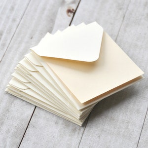 Peut inclure: Une pile d'enveloppes ivoire avec une enveloppe blanche sur le dessus. Les enveloppes sont pli&eacute;es et pr&ecirc;tes &agrave; &ecirc;tre utilis&eacute;es pour envoyer des lettres ou des cartes.