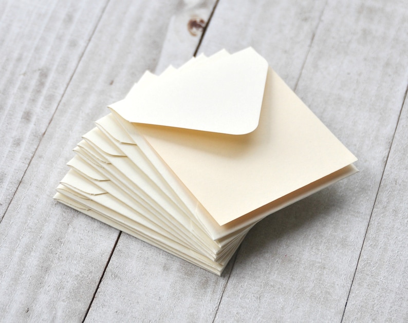 Peut inclure: Une pile d'enveloppes ivoire avec une enveloppe blanche sur le dessus. Les enveloppes sont pli&eacute;es et pr&ecirc;tes &agrave; &ecirc;tre utilis&eacute;es pour envoyer des lettres ou des cartes.