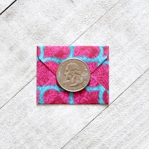 May include: A pink and blue patterned envelope with a silver US quarter coin on top.