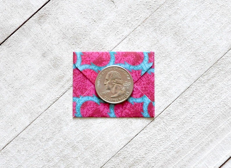 May include: A pink and blue patterned envelope with a silver US quarter coin on top.