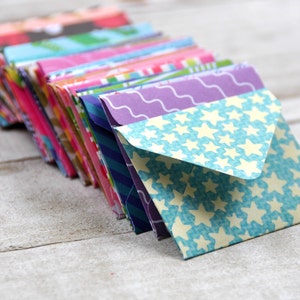 May include: A stack of colorful patterned envelopes with a blue envelope with white stars on top.