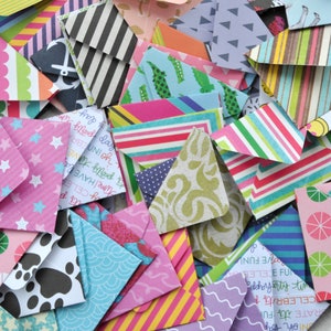 May include: A collection of colorful patterned paper envelopes, some with stars, polka dots, stripes, and other designs. The envelopes are arranged in a pile on a white surface.