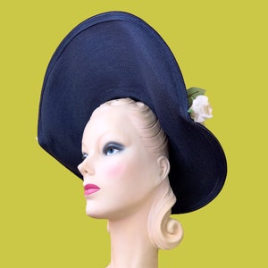May include: A large, wide-brimmed navy blue hat with a white flower accent. The hat is worn by a mannequin with blonde hair.