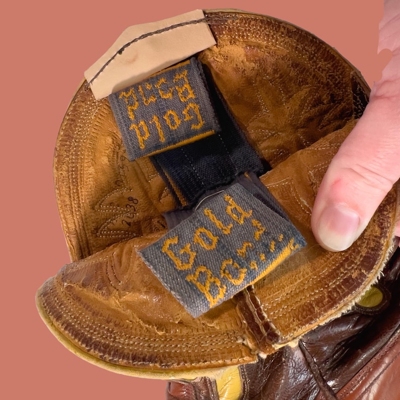May include: Close-up of a brown leather cowboy boot. The boot's interior reveals a label that reads "Gold Bond" in yellow lettering on a gray background. The boot has a worn, textured appearance.