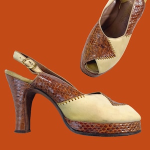 May include: Vintage high-heeled slingback shoes. The shoes feature a brown snakeskin pattern on the heel and upper, with a cream-colored suede panel. The platform sole and heel are approximately 3 inches (7.6 cm) high.