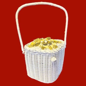May include: White wicker basket with a handle, adorned with gold-colored seashell and pearl embellishments on the lid. The basket has a rectangular shape and a woven texture, perfect for carrying items.