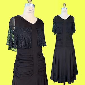 May include: Two black dresses on dress forms. The dresses have a V-neck and lace detailing on the shoulders. The dress on the left has a ruched bodice. The dress on the right has a flowing skirt. Both dresses are vintage.