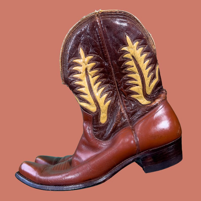 May include: A brown and tan cowboy boot with a pointed toe. The boot features decorative yellow stitching and a leather upper. The boot is approximately 12 inches tall.