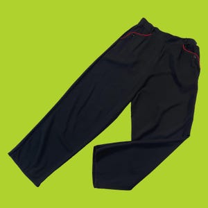 Puede incluir: Pantalones negros con ribete rojo sobre un fondo verde lima. Los pantalones tienen un diseño de pierna recta y dos botones en la cintura. Los pantalones están hechos de un material suave y fluido.