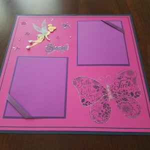 May include: Pink scrapbook page with a Tinkerbell illustration, a butterfly with the text "Tink" and the words "Faith, trust & pixie dust". There are two purple photo spaces with a purple ribbon on the left side.