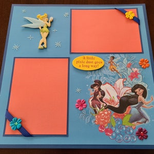May include: A scrapbook page with a blue background and two orange picture frames. The page features a Tinkerbell character, flowers, and the text "A little pixie dust goes a long way!"