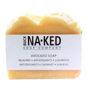 Puede incluir: Una pastilla de jab&oacute;n de aguacate de Buck Naked Soap Company. El jab&oacute;n es de color amarillo claro y tiene una etiqueta blanca con el nombre de la empresa y la informaci&oacute;n del producto. La etiqueta dice "Buck Naked Soap Company, Avocado Soap, Relaxing, Antioxidants, Luxurious, Antioxydants, Calmantes, Luxueux."