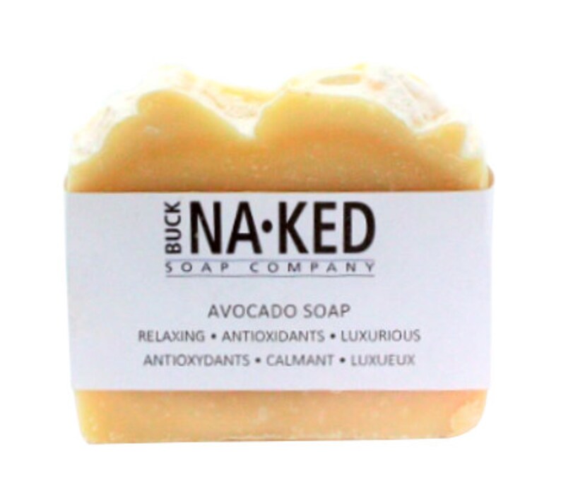 Puede incluir: Una pastilla de jab&oacute;n de aguacate de Buck Naked Soap Company. El jab&oacute;n es de color amarillo claro y tiene una etiqueta blanca con el nombre de la empresa y la informaci&oacute;n del producto. La etiqueta dice "Buck Naked Soap Company, Avocado Soap, Relaxing, Antioxidants, Luxurious, Antioxydants, Calmantes, Luxueux."