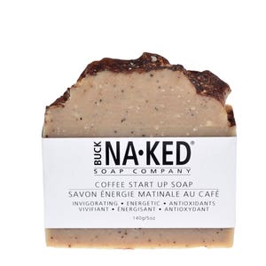 May include: A brown and beige bar of soap with the text "BUCK NA-KED SOAP COMPANY" and "COFFEE START UP SOAP" printed on the label. The label also includes the text "SAVON &Eacute;NERGIE MATINALE AU CAF&Eacute;" and "INVIGORATING &bull; ENERGETIC &bull; ANTIOXIDANTS VIVIFIANT &bull; ENERGISANT &bull; ANTIOXYDANT" in French. The soap is 140g/5oz.
