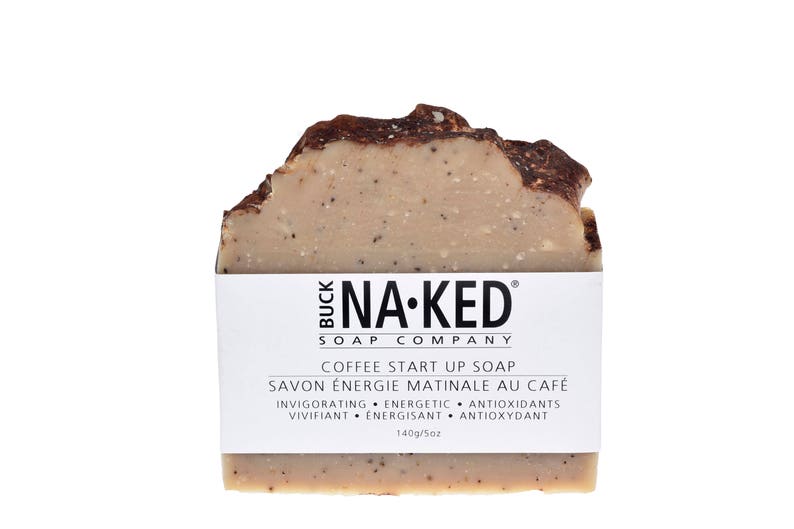 May include: A brown and beige bar of soap with the text "BUCK NA-KED SOAP COMPANY" and "COFFEE START UP SOAP" printed on the label. The label also includes the text "SAVON &Eacute;NERGIE MATINALE AU CAF&Eacute;" and "INVIGORATING &bull; ENERGETIC &bull; ANTIOXIDANTS VIVIFIANT &bull; ENERGISANT &bull; ANTIOXYDANT" in French. The soap is 140g/5oz.