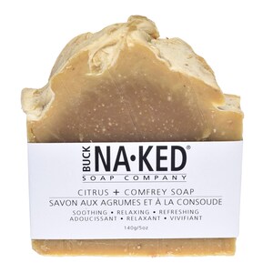 Może przedstawiać: Kostka mydła w jasnobrązowym kolorze o teksturowanej powierzchni. Mydło ma białą etykietę z napisem "BUCK NA-KED SOAP COMPANY" i "CITRUS + COMFREY SOAP". Etykieta zawiera r&oacute;wnież tekst "SOOTHING &bull; RELAXING &bull; REFRESHING" i "140g/5oz".