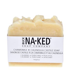 May include: A bar of white soap with the text "NA-KED SOAP COMPANY" and "CHAMOMILE + CALENDULA CASTILE SOAP" printed on the label. The soap is labeled as calming, purifying, and peaceful.
