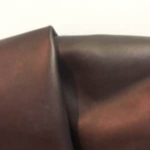 Pode incluir: Close-up de um tecido de couro marrom escuro. O couro tem uma superfície lisa e ligeiramente brilhante.