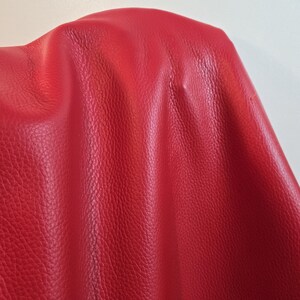 Può includere: Un materiale rosso vibrante con una distinta consistenza granulosa. La superficie mostra pieghe e grinze naturali, creando riflessi e ombre sulla grana. Il materiale appare flessibile e morbido, con un colore rosso intenso e uniforme.