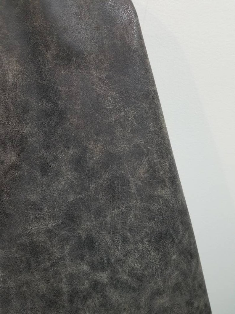 Op de afbeelding: Close-up van een donkergrijze, textuurrijke stof met een licht verweerde uitstraling. De stof heeft een subtiele glans en een licht ruw gevoel.