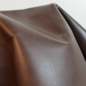 May include: Close-up of a brown leather fabric with a smooth, slightly textured surface.