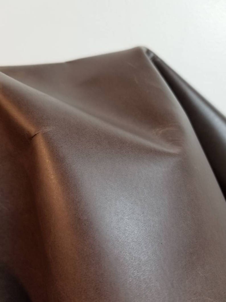 May include: Close-up of a brown leather fabric with a smooth, slightly textured surface.