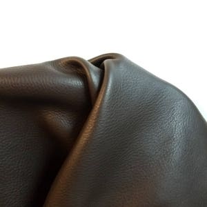 Pode incluir: Close-up de um pedaço de couro marrom escuro. O couro está dobrado e tem uma superfície texturizada.