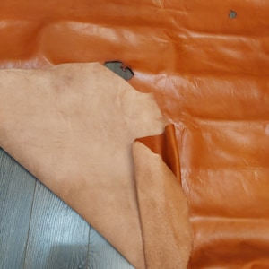 Pode incluir: Um pedaço de couro marrom com um forro de camurça marrom mais claro. O couro está dobrado e a camurça é visível.