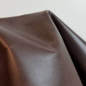 May include: A close-up of a brown leather fabric. The fabric has a smooth, slightly shiny surface.