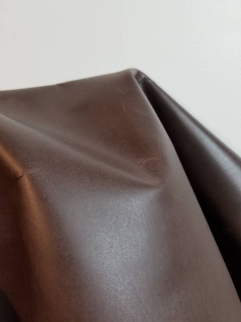 May include: A close-up of a brown leather fabric. The fabric has a smooth, slightly shiny surface.