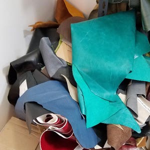May include: A pile of leather scraps in various colors, including teal, blue, brown, black, and red. The scraps are arranged in a random order and some are folded.