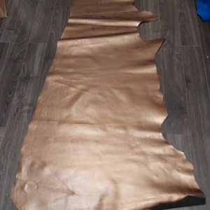 Pode incluir: Uma grande peça de couro marrom com um acabamento liso e brilhante. O couro está dobrado e colocado em um piso de madeira.