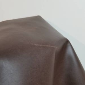 May include: A close-up of a brown leather surface with a slight crease. The leather has a smooth, textured appearance.